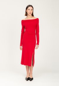 Rotes schulterfreies Kleid mit langen Ärmeln, geripptem Ausschnitt, tailliertem Oberteil und hoher Schlitz bis zum Oberschenkel; kombiniert mit schwarzen spitzen Schuhen.