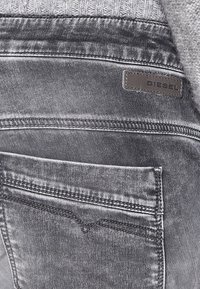 Gray denim jeans featuring a back pocket with a subtle V-shaped stitch detail, complemented by a leather Diesel brand tag.