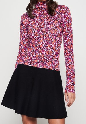 Vrouw draagt een langarmige, roze-paarse bloemmotief coltop gecombineerd met een zwarte uitlopende rok, afgeknipt halverwege de dij.