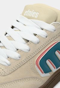 Μπεζ σουέτ αθλητικά παπούτσια με λευκές κορδόνες και επενδεδυμένη γλώσσα. Διαθέτει πολύχρωμο λογότυπο σε τυρκουάζ, ροζ και λευκό. Καουτσούκ σόλα με υφές.