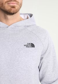 Sudadera gris hecha de tela suave con mangas raglán. Presenta un logo negro de "The North Face" en el lado izquierdo del pecho.