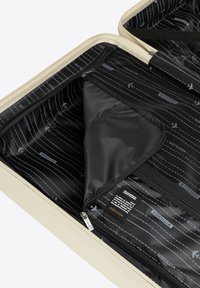 Harde koffer in crèmekleur met een zwarte binnenkant. Voorzien van een met rits sluitende scheiding en een stoffen label, met een gevoerde binnenkant met een patroon van vliegtuigmotieven.