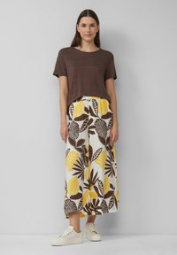 Haut marron à manches courtes associé à une jupe blanche ornée de motifs de feuilles jaunes et brunes. Des baskets beiges complètent la tenue.