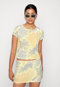 Conjunto de top cropped e saia mini com padrão floral amarelo e lavanda, feito de tecido suave com uma textura lisa, mangas curtas e um design ajustado.