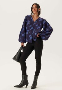 Marinblus med stora puffärmar, blommönster i blått, knappstängning framtill. Matchad med svarta skinny jeans och ankelboots.