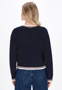 Marine gebreide trui met kabelpatroon, contrasterende crèmekleurige en kastanjebruine gestreepte halslijn en zoom. Lange mouwen en slim fit stijl.