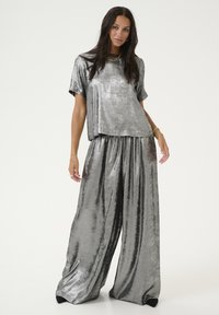 Ensemble en métal argenté en deux pièces comprenant un t-shirt ample et un pantalon large, tous deux avec une texture lisse et réfléchissante.