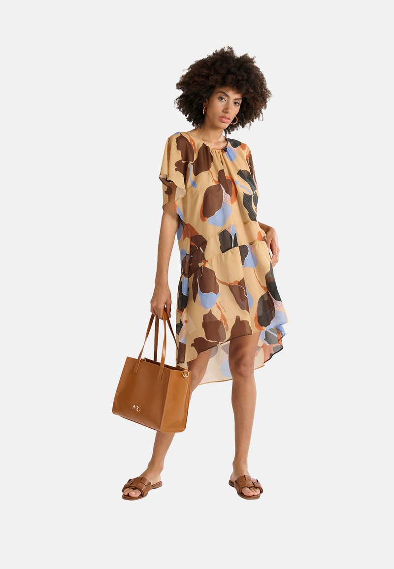 Robe beige transparente à motif floral, avec des manches courtes et un ourlet irrégulier. Sac tote en cuir beige avec double poignée et logo. Sandales à glissière marron.