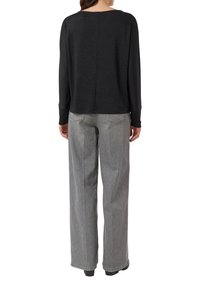 Czarny dzianinowy top z długim rękawem o luźnym kroju i szerokim dekolcie, zestawiony z jasnoszarymi, luźnymi dżinsami z wysokim stanem.