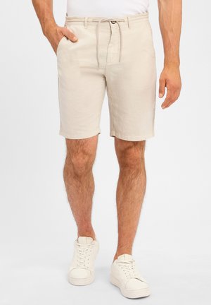 Beige Leinen-Shorts mit einem Kordelzugbund, Seitentaschen und umgeschlagenen Säumen, kombiniert mit weißen Sneakers.