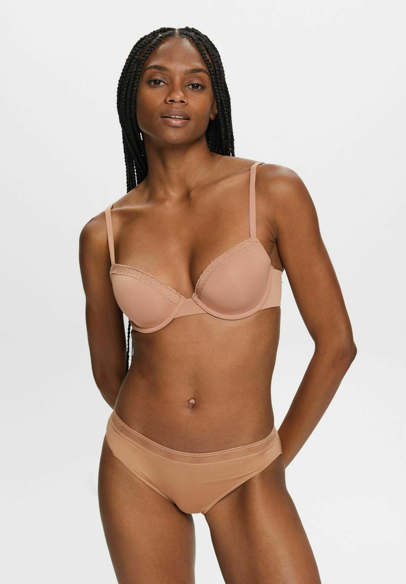Beige Unterwäsche-BH mit Spitzenrand und verstellbaren Trägern, kombiniert mit passendem nahtlosen Bikini-Höschen. Glattes Material, leicht glänzende Oberfläche.