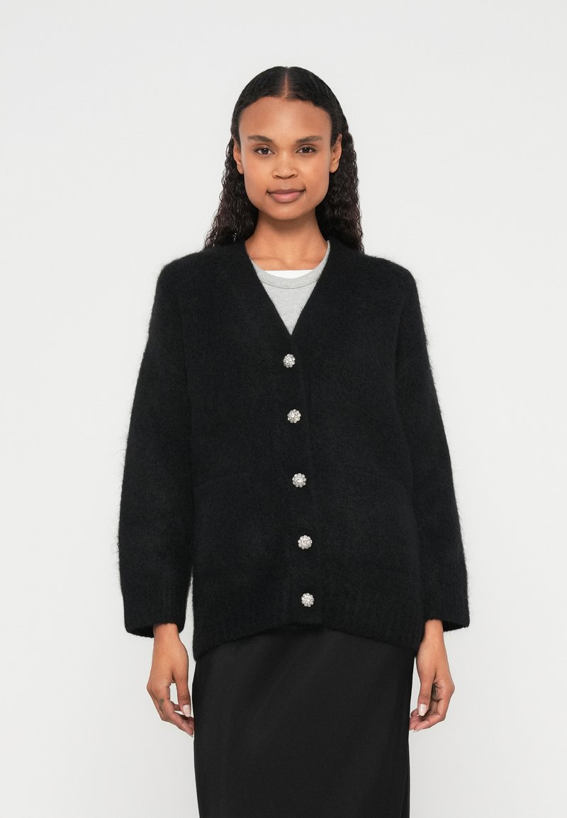 Μαύρη, χνουδωτή ζακέτα με V-λαιμόκοψη, που διαθέτει πέντε διακοσμητικά κουμπιά σε σχήμα πολύτιμου λίθου κατά μήκος του μπροστινού μέρους και δύο τσέπες. Μαλακή υφή, άνετη εφαρμογή.