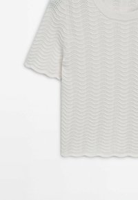 Haut en maille blanche à manches courtes avec des motifs verticaux ondulés et ponctués texturés sur un fond uni.