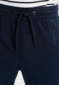 Navy blue casual pants with a stretchy waistband, adjustable drawstring, and a single front pocket detail. Soft fabric texture.