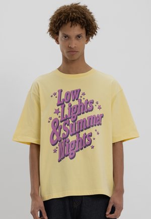Gelbes Baumwoll-T-Shirt im übergroßen Schnitt. Mit lila Schriftzug "Low Lights & Summer Nights", umgeben von kleinen Sternen.