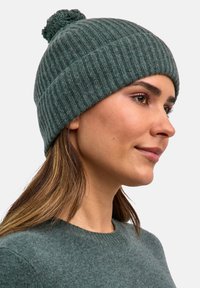 Cappello beanie in maglia a coste di colore verde scuro, con una finitura testurizzata e un pompon arrotondato sulla parte superiore, che offre una vestibilità aderente e calore.