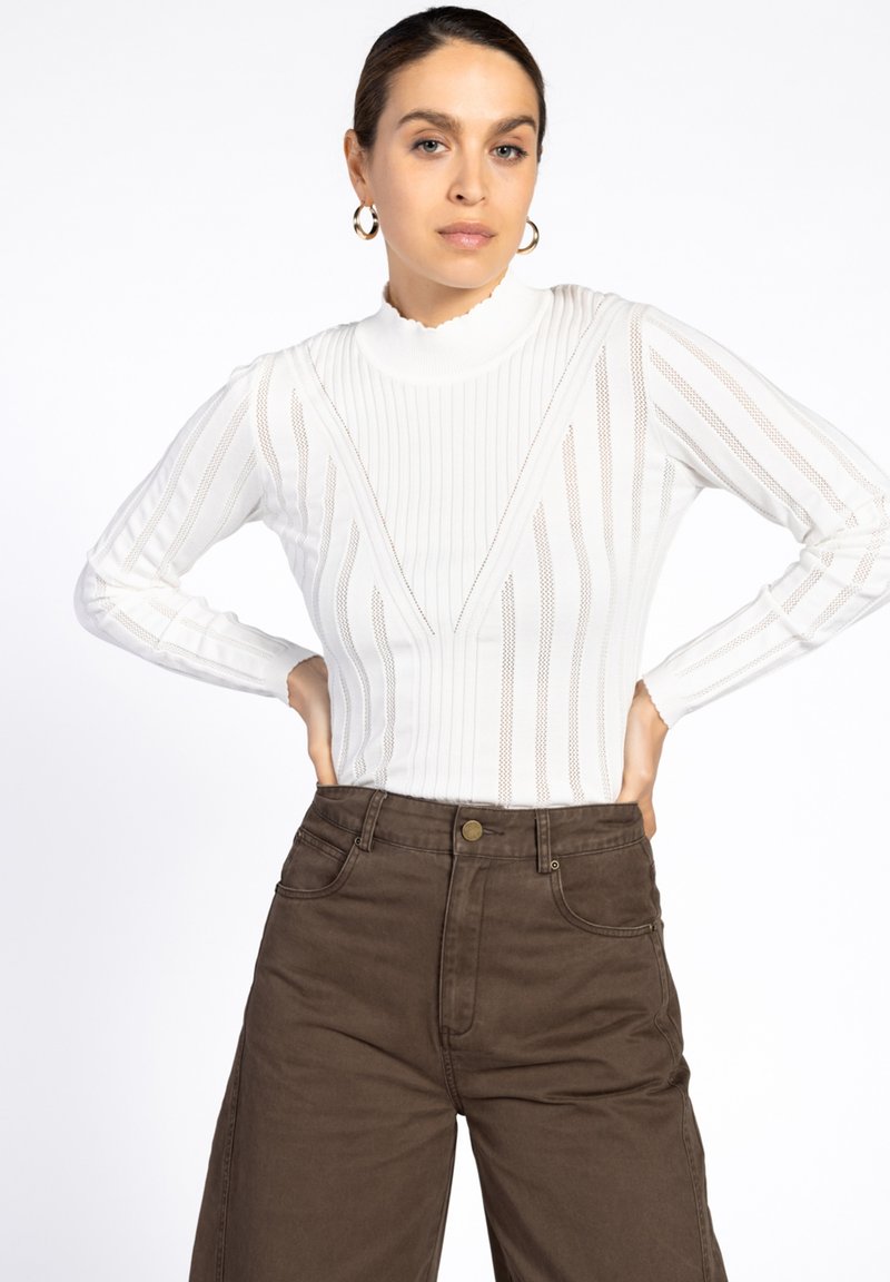 Witte geribde top met een scalloped halslijn en V-vormig ontwerp. Lange mouwen hebben verticale strepen, gecombineerd met bruine hoge taille broek.