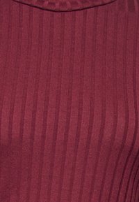 Mörkröd ribbad stickad tyg som visar vertikala strukturerade ränder och en vikt kant där uppe.