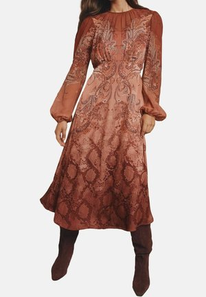 Langærmet kjole i rustfarvet med indviklede blomster- og slangeskindsmønstre, kombineret med matchende mørkebrune knælange støvler.