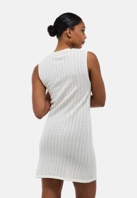 Robe sans manches en tricot blanc avec un motif texturé et des accents de couleur subtils, présentant un décolleté arrondi et une silhouette ajustée.