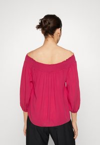 Top off-the-shoulder con maniche a palloncino di un vivace rosa, caratterizzato da un collo arricciato, una vestibilità morbida e un tessuto testurizzato.