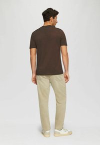 Brown short-sleeved t-shirt, cotton material, relaxed fit, paired with light beige pants and neutral sneakers. Simple design with no patterns.
