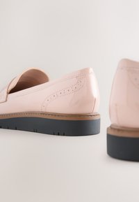 Paire de mocassins en cuir verni rose clair avec semelles noires et perforations décoratives sur une surface blanche.