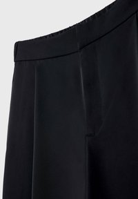 Zwarte broek van gladde stof met een elastische tailleband, voorzien van een zijzak en een wijde pijpdesign.