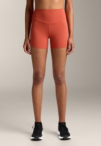 Magasan szabott, testhezálló, rozsdabarna rövidnadrág rugalmas anyagból, sima derékkal és varrás részletekkel. Aktív viseletre alkalmas.