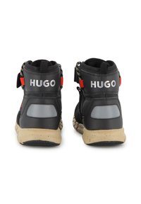 Sneakers alte nere con logo bianco "HUGO", accenti rossi, colletto imbottito, dettagli grigi riflettenti e suola in gomma testurizzata.