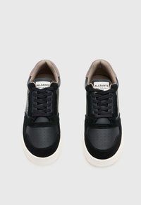 Ζευγάρι μαύρων και γκρι αθλητικών παπουτσιών AllSaints με λευκές σόλες και μαύρα κορδόνια, από άνωθεν θέα σε ανοιχτό γκρι φόντο.