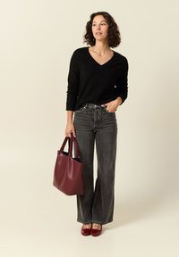 Maglione nero a V, jeans in denim grigi alto in vita, borsa a tracolla in pelle bordeaux e scarpe rosse lucide. Design minimalista e vestibilità casual.