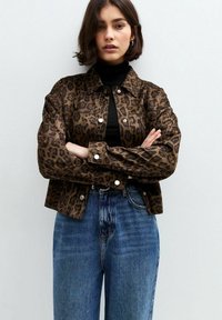 Leopardenmuster-Denimjacke mit Druckknöpfen; kombiniert mit einem schwarzen Rollkragenpullover und blauen hoch taillierten Jeans, die ein kurzes Design zeigen.