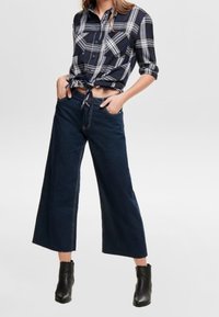 Mörkblå rutigt button-up skjorta, knuten i midjan, kombinerad med högmidjade vida jeans i mörk denim och svarta stövletter med klack.