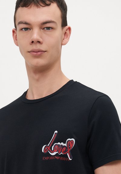 T-shirt nera a maniche corte in cotone con collo tondo. Presenta una grafica colorata "Love" e il testo "Emporio Armani" sul lato sinistro.