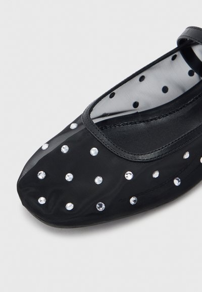 Μαύρη επίπεδη Mary Jane με διαφανές μπροστινό μέρος καλυμμένο με μικρές στρογγυλές στρας και εσωτερική επένδυση από πουά δίχτυ.
