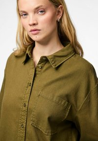 Olivgrön knapp-up skjorta tillverkad av texturerad tyg, med krage, en framficka och en avslappnad passform.