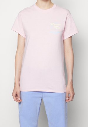 Vrouw in een lichtroze t-shirt met de tekst "Casa Mamma Mia On Vacation Club" op de borst, gecombineerd met lichte blauwe broek.