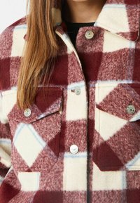 Czerwona i kremowa sztruksowa koszula w kratę z dużym wzorem w kratę, z metalowymi klamrami i dwoma przednimi kieszeniami. Miękka tekstura.