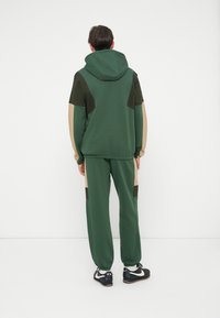 Vihreä huppari hupulla ja värijakolla, yhdistettynä vihreisiin collegehousuihin, joissa on ruskeita ja beigestä sävyjä.