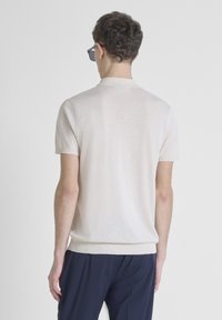 Licht beige gebreide trui met korte mouwen, een ribbelboord bij de hals en aan de onderkant, gecombineerd met marineblauwe broek. Gladde textuur; geen zichtbare patronen of accenten.