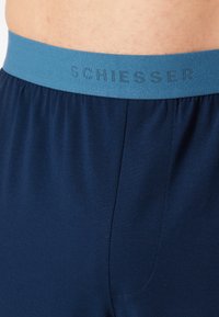 Mutande blu navy con un elastico azzurro chiaro recante il testo "SCHIESSER." Tessuto liscio con una morbida texture e dettagli delle cuciture.