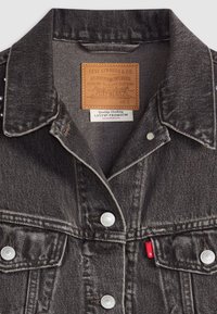Black denim Levi's jacket with metal buttons, two chest pockets, and brown leather label inside collar showing brand and size S.