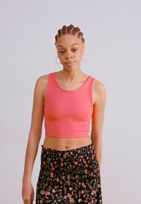Jasnoróżowy prążkowany crop top z okrągłym dekoltem, w połączeniu z czarną spódnicą w kwiatowy wzór i marszczoną talią.