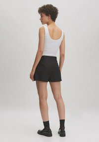 Witte geribde tanktop gecombineerd met zwarte hoge shorts. De shorts hebben een nette afwerking met zijzakken en een klassieke snit.