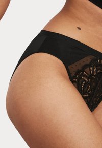 Svart lingerie med en blandning av slät och genomskinlig mesh, prydd med spetsblommönster som framhäver en intrikat design och textur.