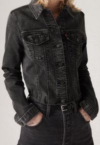 Musta farkkutakki nappikiinnityksellä, jossa on kaksi rintaremmipussi ja terävä kaulus. Ominaisuuksiin kuuluu haalistunut pinta ja hopeiset yksityiskohdat.