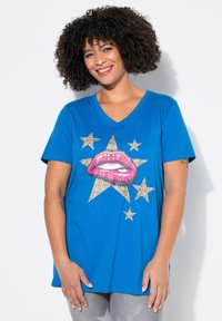 Camiseta de algodón azul con un gráfico de labios rosas y detalles goteantes, además de estrellas de leopardo doradas. Diseño de escote en V y mangas cortas.