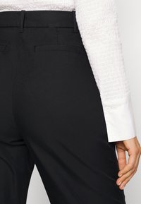 Svarta skräddarsydda byxor med en slät yta, har en slim fit, bakfickor och hög midja, kombinerat med en vit skjortärm.