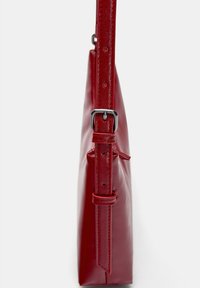 Red, glossy leather shoulder bag with a slim shape, adjustable strap, and silver buckle detail. Features minimalistic design and no visible hardware.